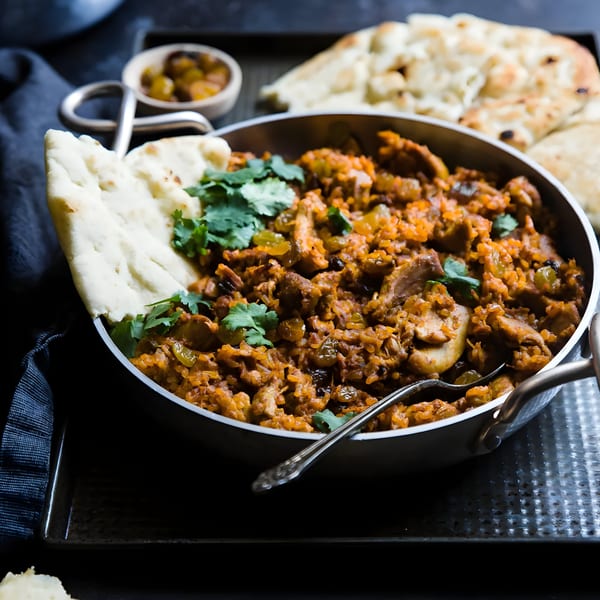 Chicken biryani with raisins and cilantro, served in a metal bowl with naan bread.