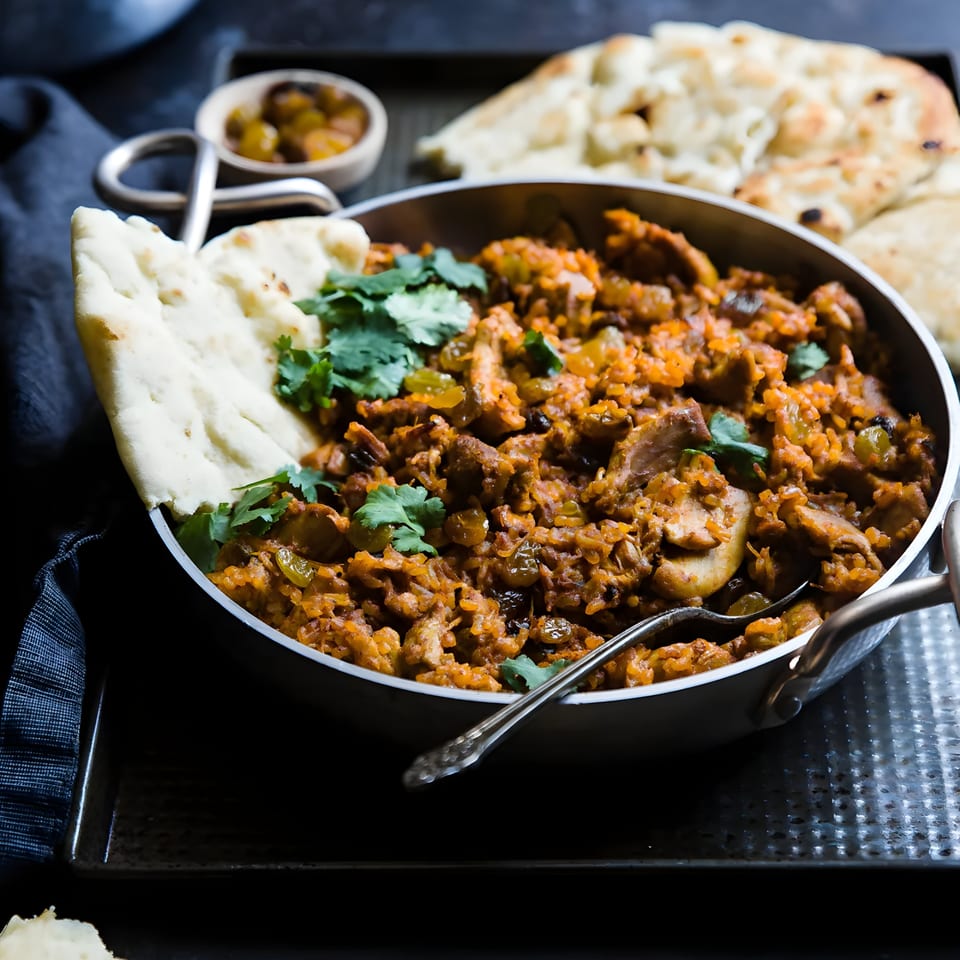 Chicken biryani with raisins and cilantro, served in a metal bowl with naan bread.