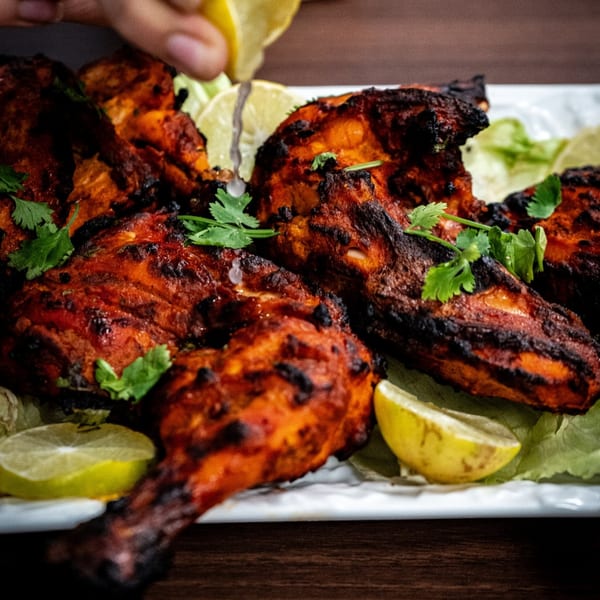 Spicy Indian tandoori chicken with cilantro and lime wedges on a white platter.
